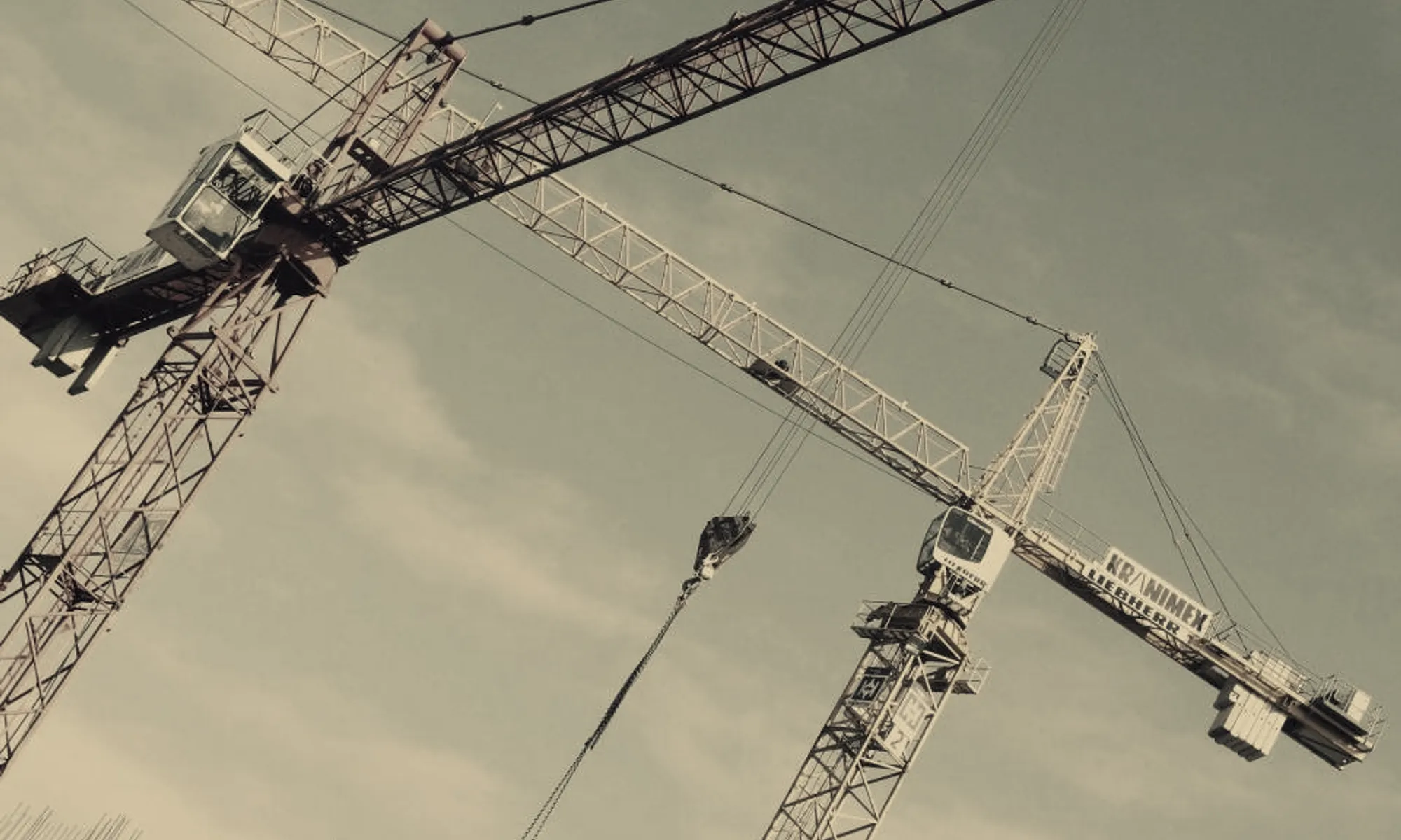 Two tower cranes against an open sky